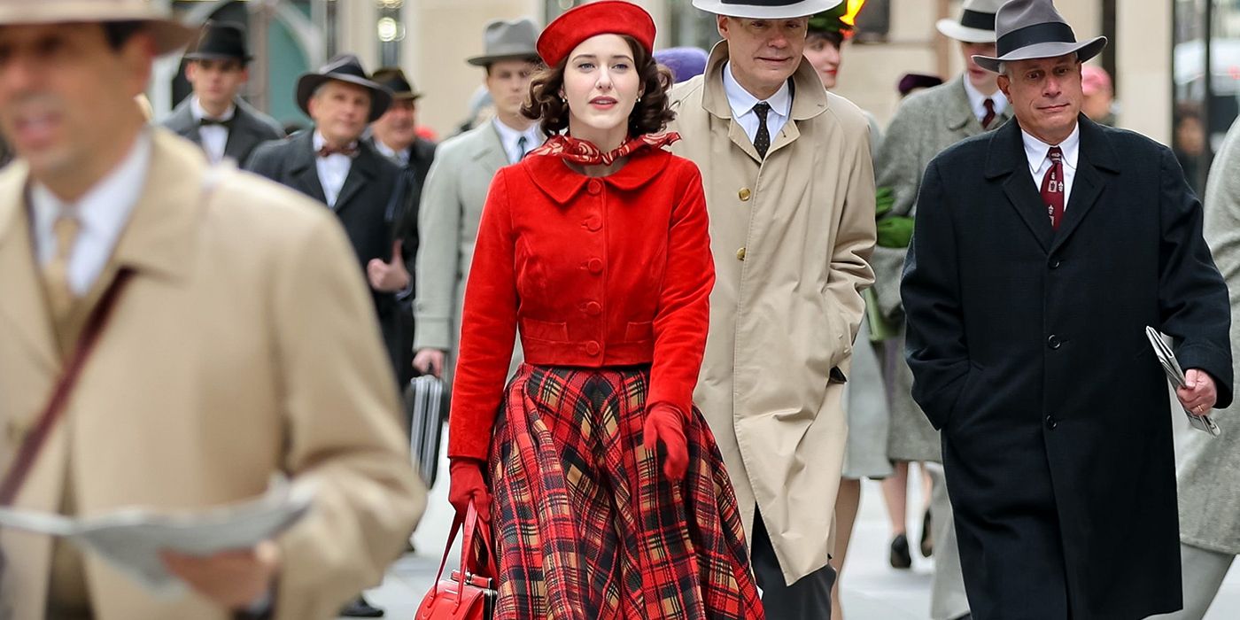 Midge Maisel from The Marvelous Mrs. Maisel walking down the street in red, surrounded by men in beige and black suits.