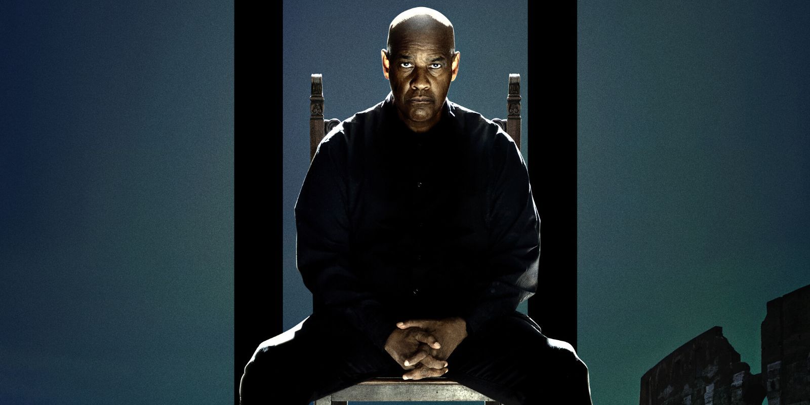 Denzel Washington in a black suit sitting on an antique chair with his hands folded