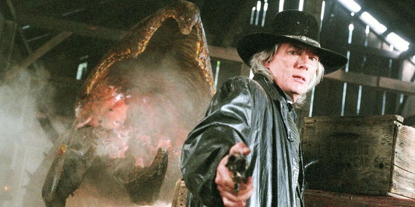 Billy Drago como Black Hand Kelly segurando uma arma com um graboid atrás dele em Tremors 4.