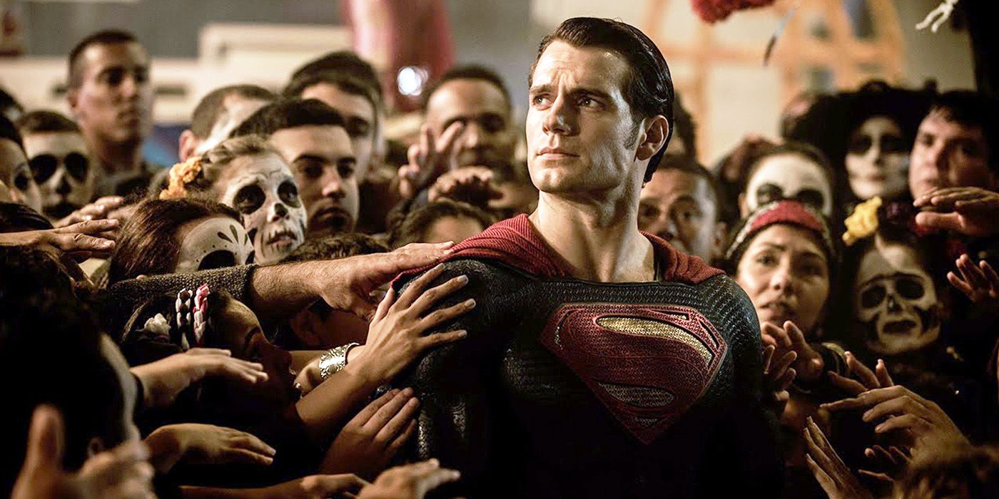 Superman stands in the middle of a crowd and looks into the sky as people reach out to touch him.