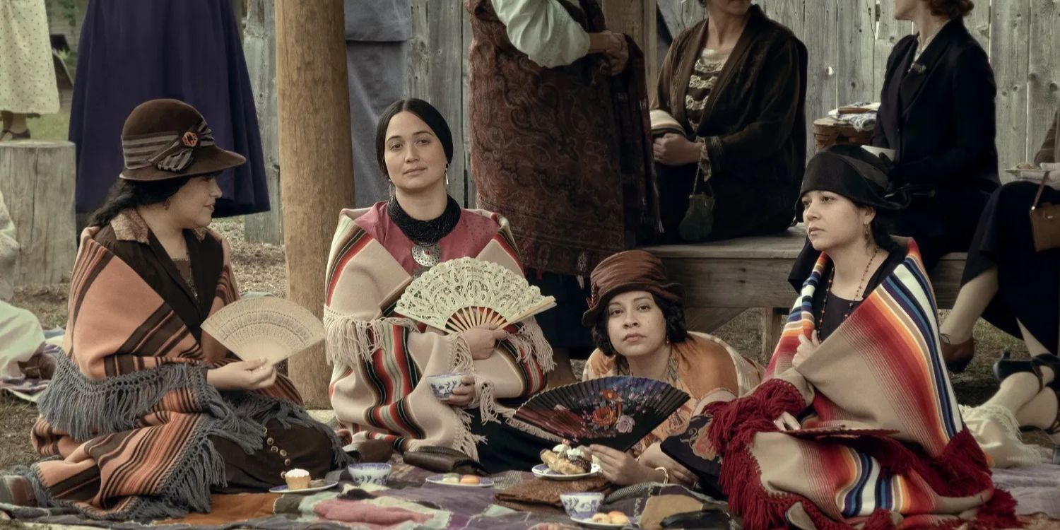 Lily Gladstone's Mollie holding a fan and sitting with other women in Killers of the Flower Moon