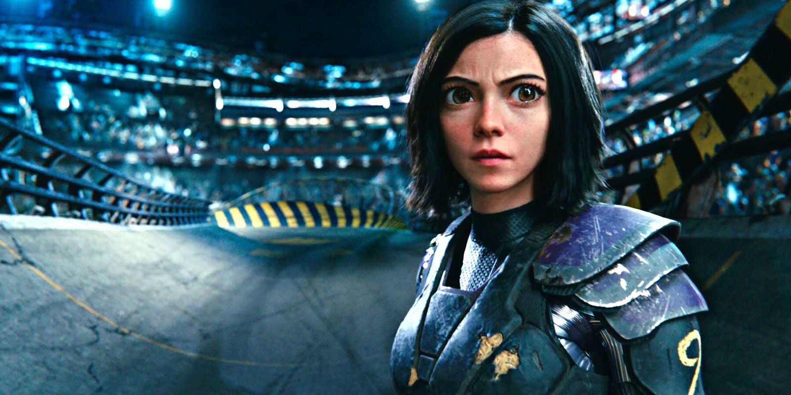 Alita concentrates while standing in a metal arena, surrounded by an audience