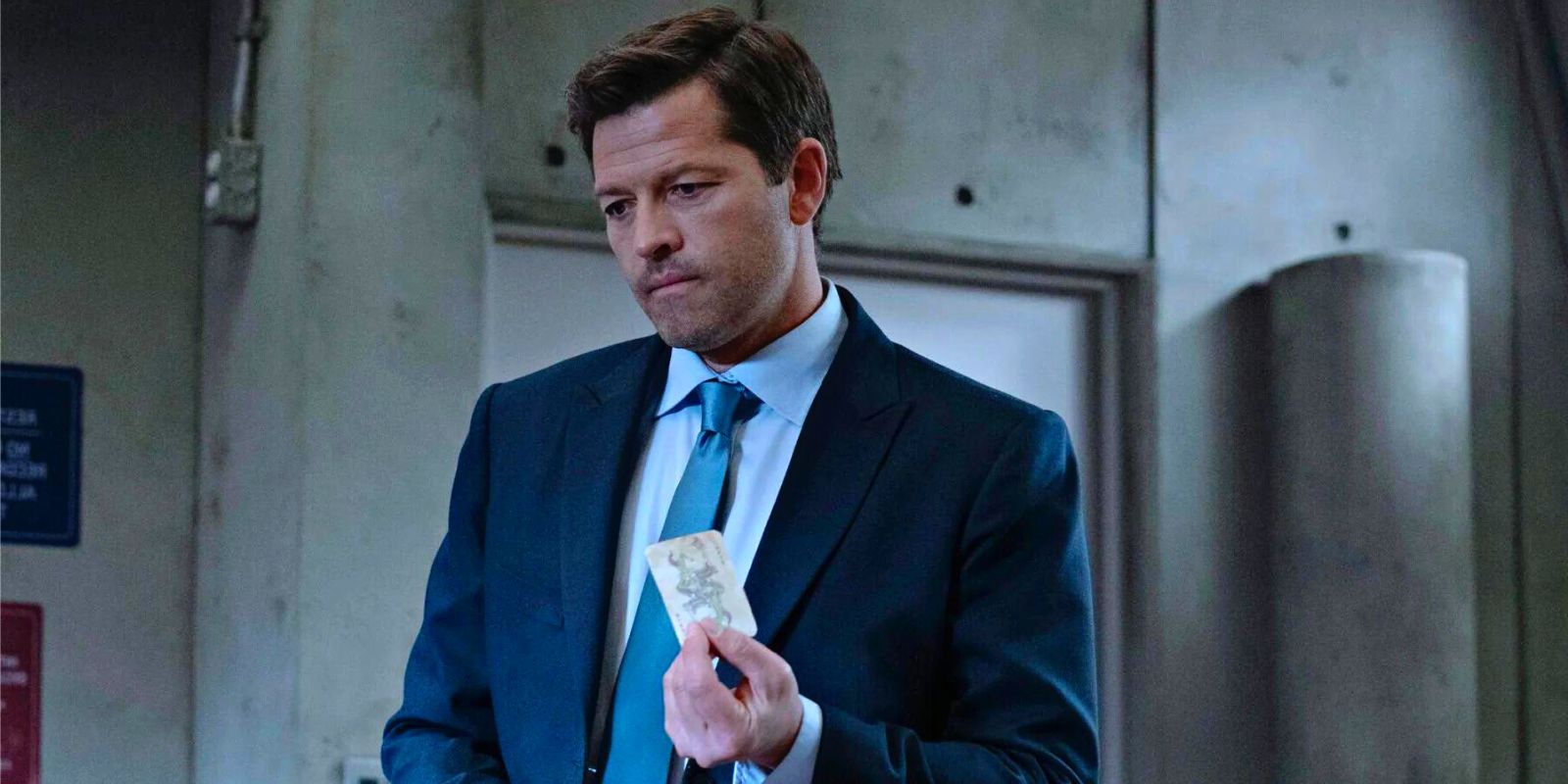 Misha Collins as Harvey Dent holds up a Joker playing card in Gotham Knights
