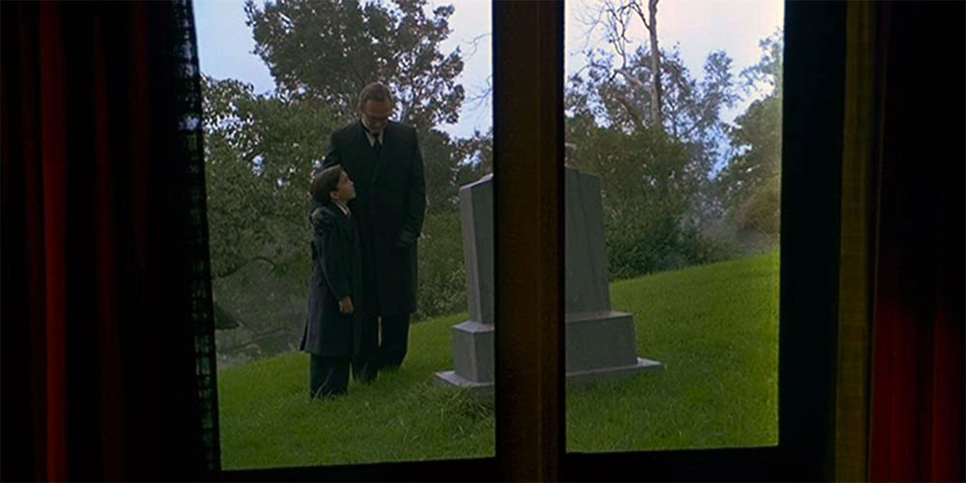 Eric Lloyd as Bruce Wayne and Jon Simmons as Alfred Pennyworth standing by a grave in Batman & Robin