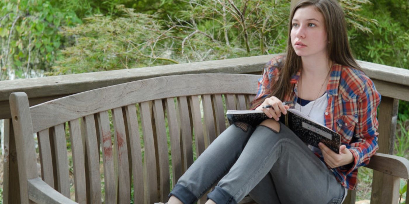 Enid (Katelyn Nacon) sitting on a bench with a notebook in The Walking Dead. 