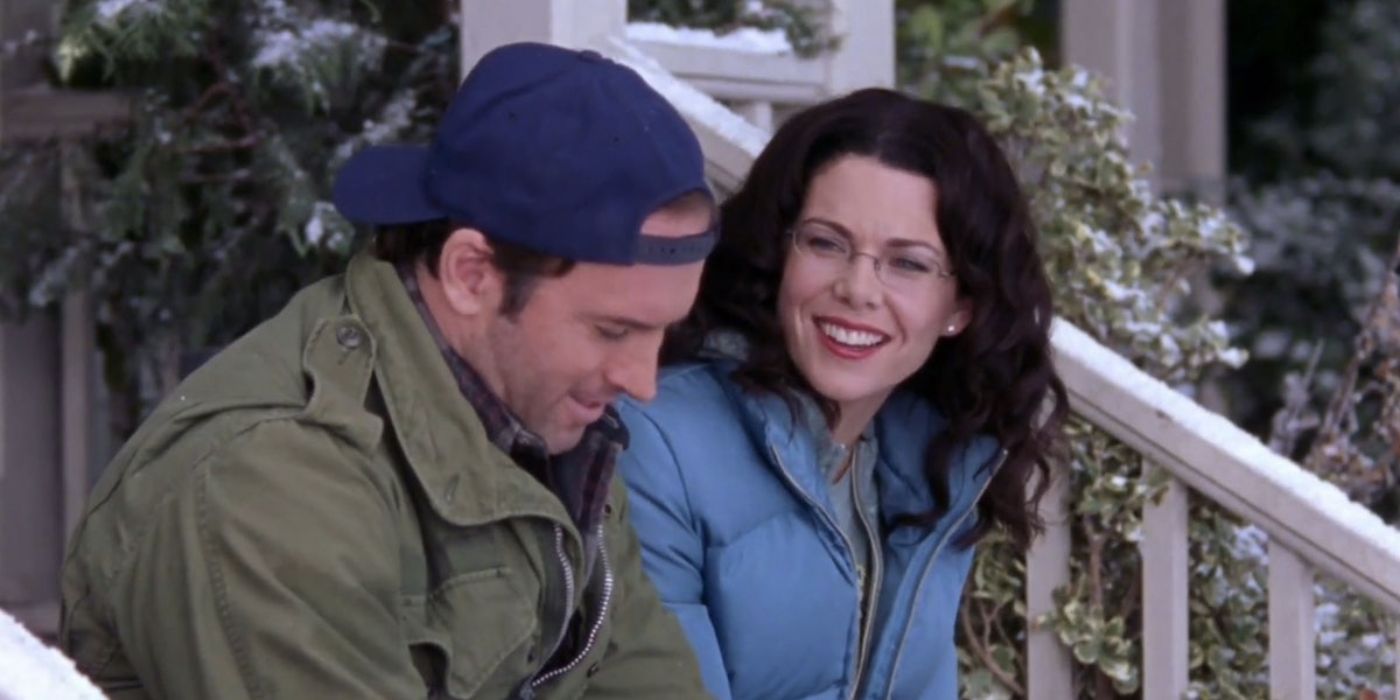Luke and Lorelai laughing while sitting on Lorelai’s snowy porch in Gilmore Girls