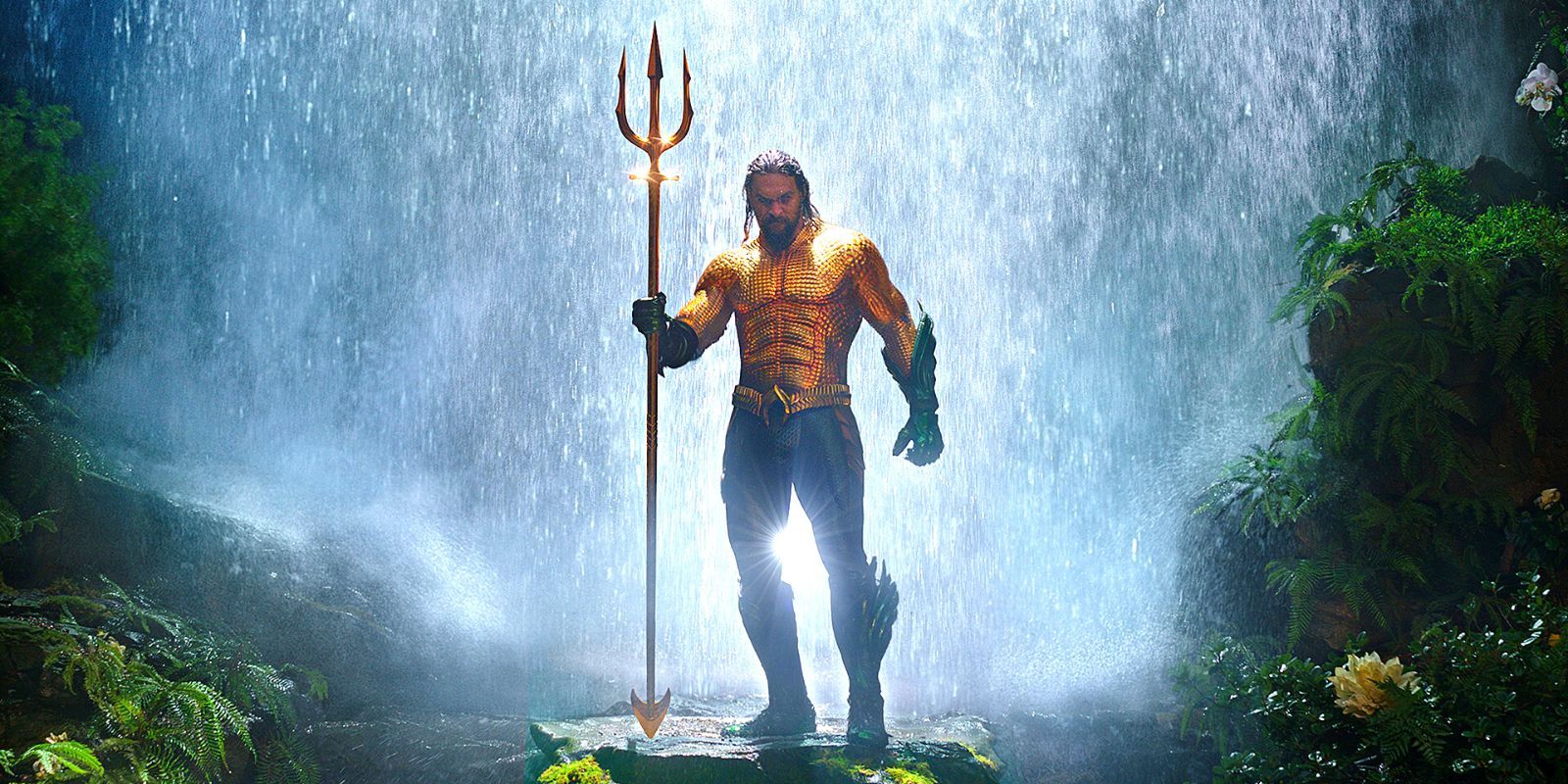 Aquaman standing with his trident under a waterfall