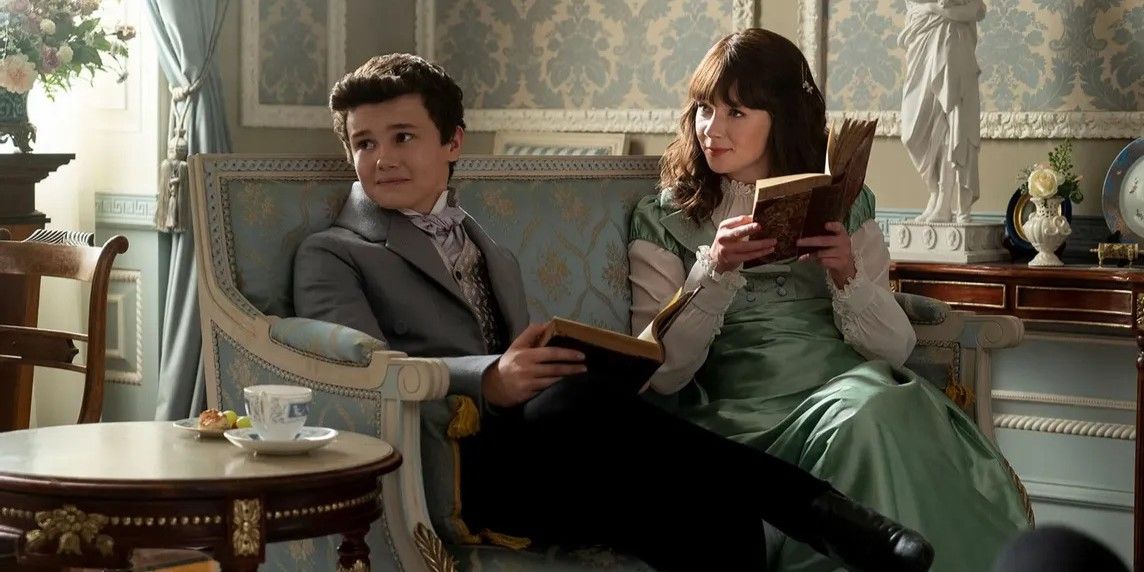 Gregory and Eloise sit on the sofa holding books while looking to their side in Bridgerton