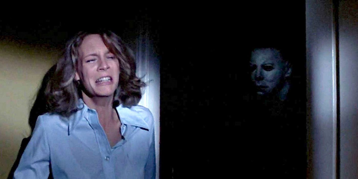 Laurie hiding around a corner, terrified with Michael Myers standing on the other side in a scene from Halloween.
