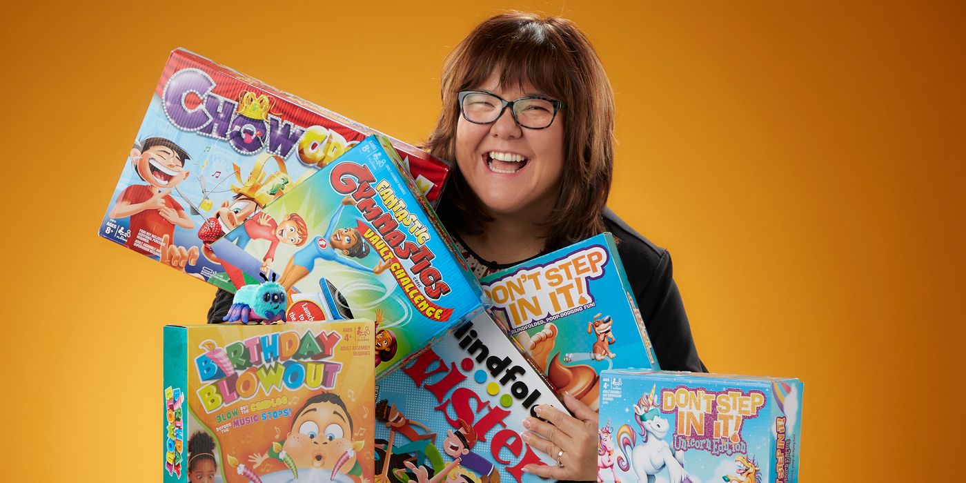 Hasbro Gaming director Tanya Thompson smiles while holding board games on an orange backdrop