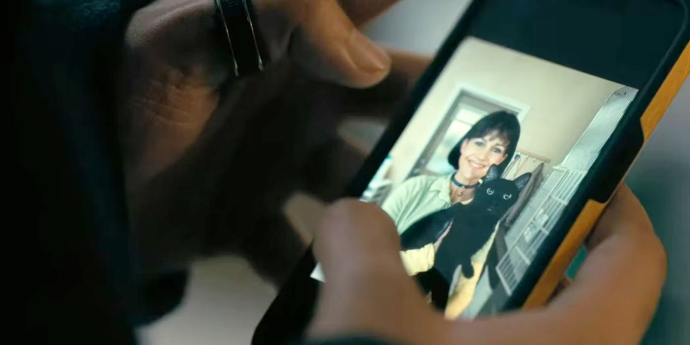 Leo looks at a picture of Verna holding the black cat on his cellphone