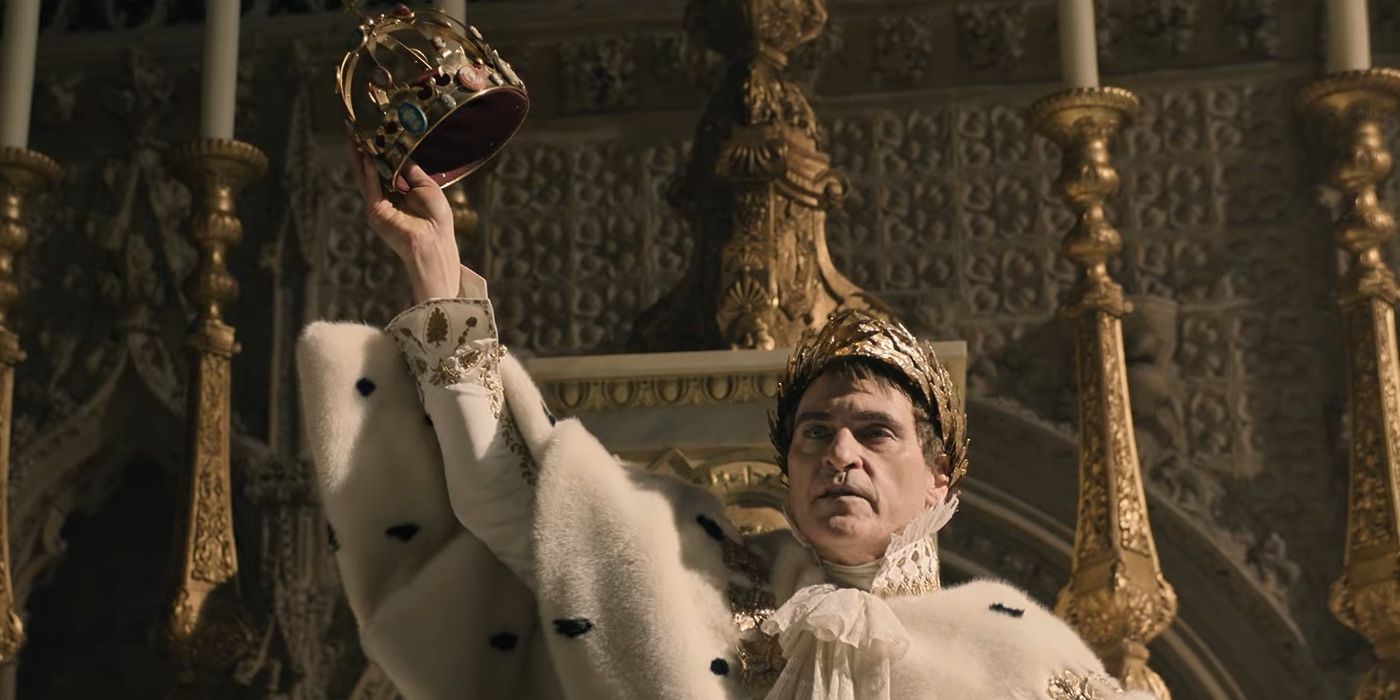 Joaquin Phoenix as Napoleon holds his crown in the air