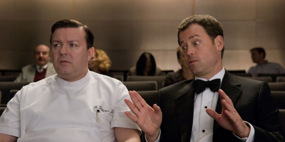 Ricky Gervais as Pincus sits next to Greg Kinnear as Frank in a lecture hall in GhostTown