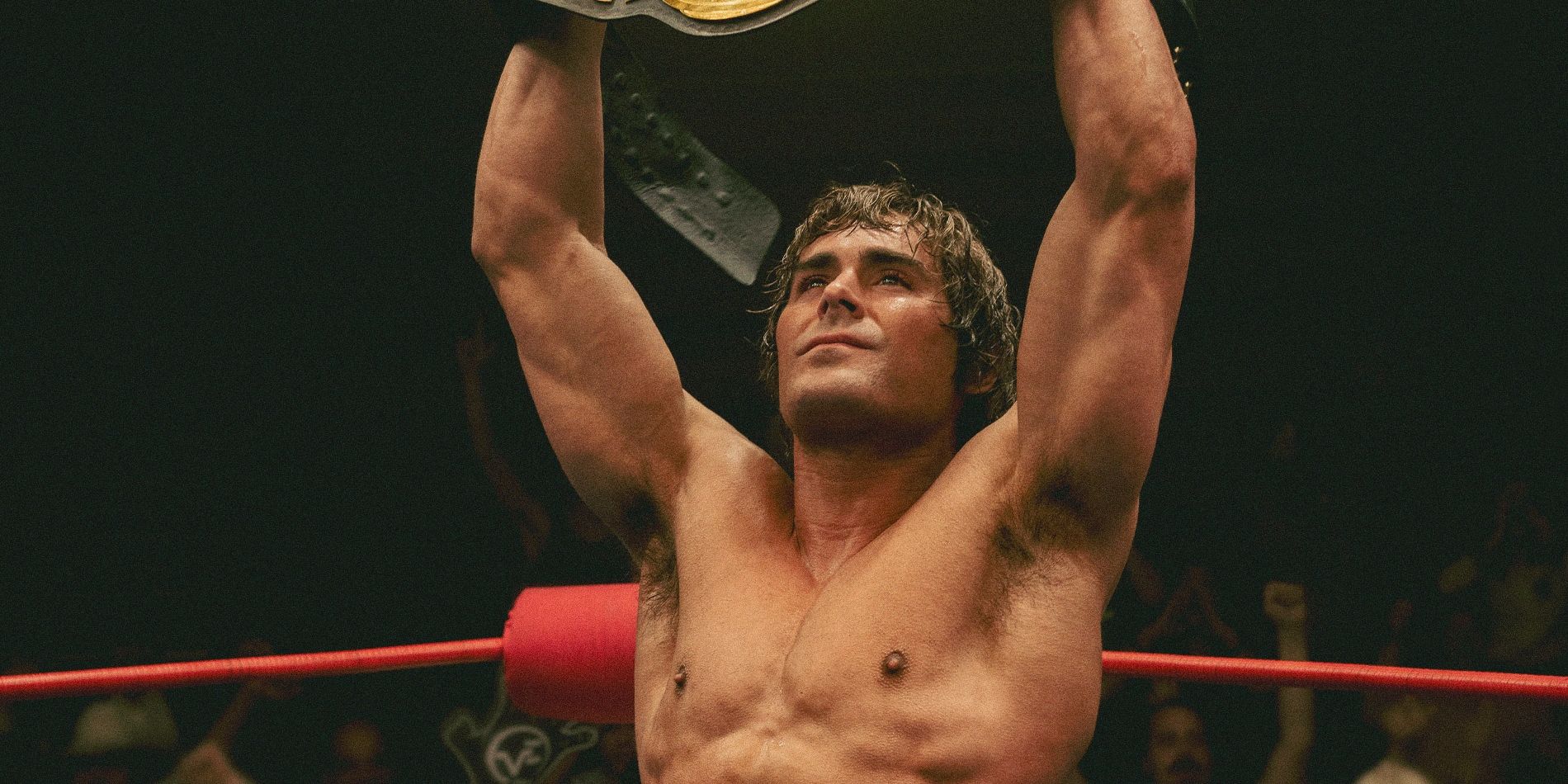 Zac Efron as wrestler Kevin Von Erich in The Iron Claw in the ring holding up a championship belt