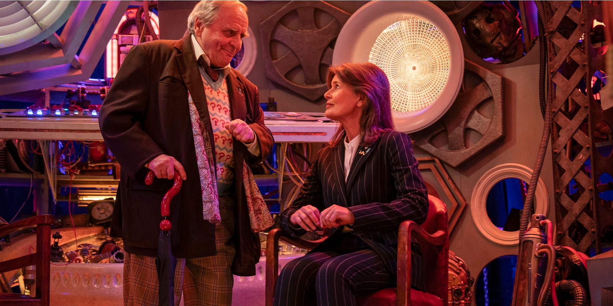 Seventh Doctor standing next to Ace, dressed in a pinstripe suit, sitting in a chair on the Memory Tardis set from Doctor Who Tales of the TARDIS