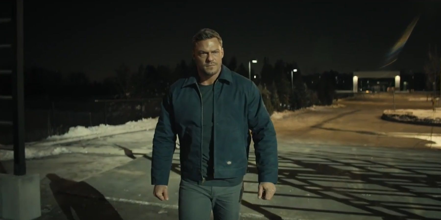Jack Reacher walking through a large metal gate with an empty parking lot behind him from Season 2
