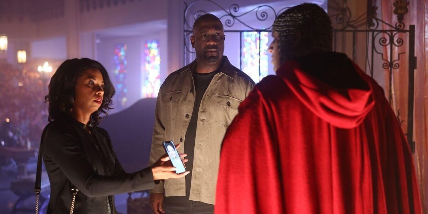 Angel Parker as Luna Grey stands with Richard T. Jones as Wade Grey showing their daughter's picture to an unidentified man in a costume on The Rookie