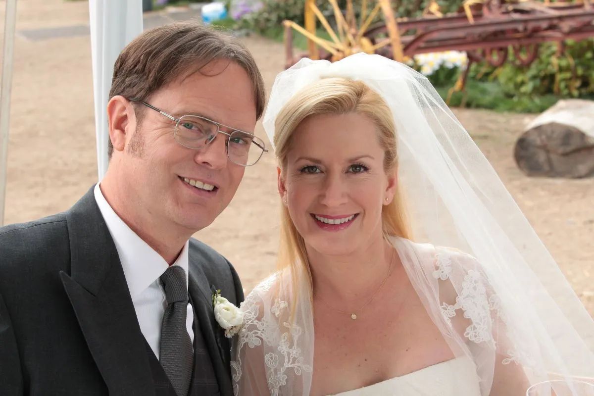 Dwight Schrute (Rainn Wilson) and Angela Martin (Angela Kinsey) smile for a photo on their wedding day in The Office