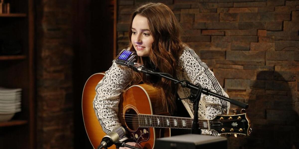 Kaitlyn Dever as Eve Baxter sitting with her guitar in front of a microphone to play a song in Last Man Standing