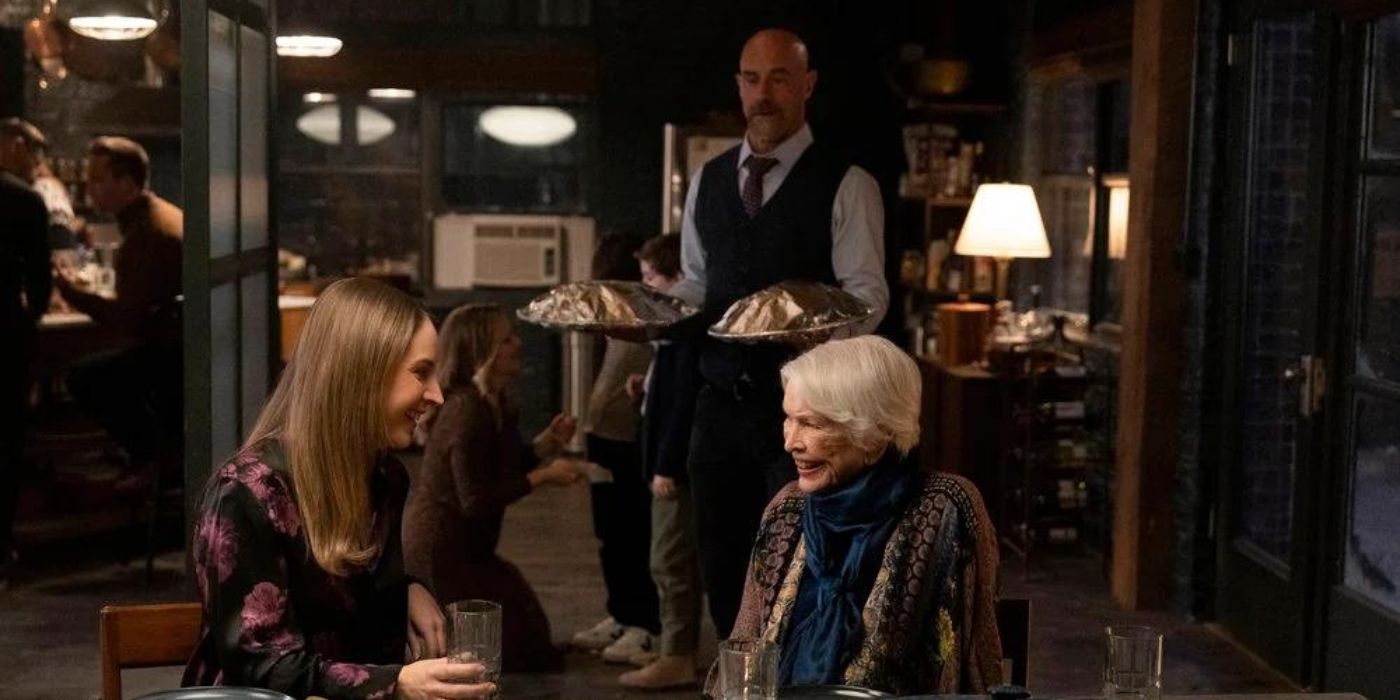 Allison Siko as Kathleen Stabler sits at a table with Ellen Burstyn as Bernie Stabler while Christopher Meloni as Elliot Stabler carries trays of food behind them on Law & Order_ Organized Crime