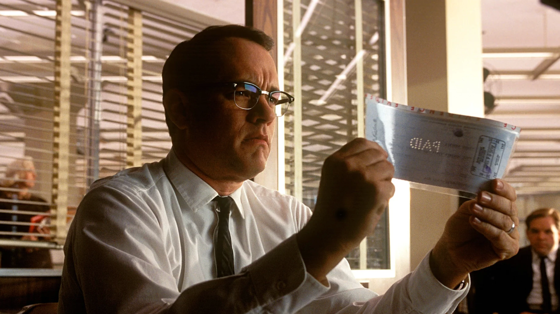 Tom Hanks examines a check in Catch Me If You Can