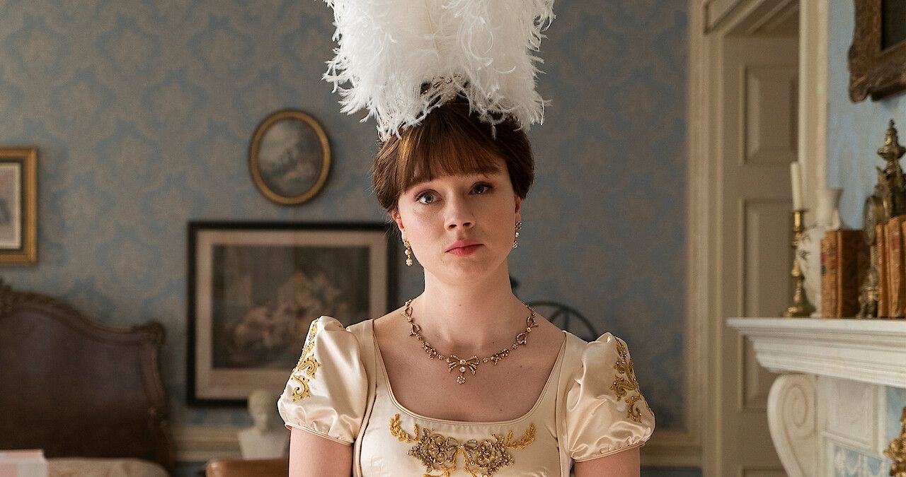 Eloise Bridgerton at her home, looks upset with a feather head piece and a formal dress.