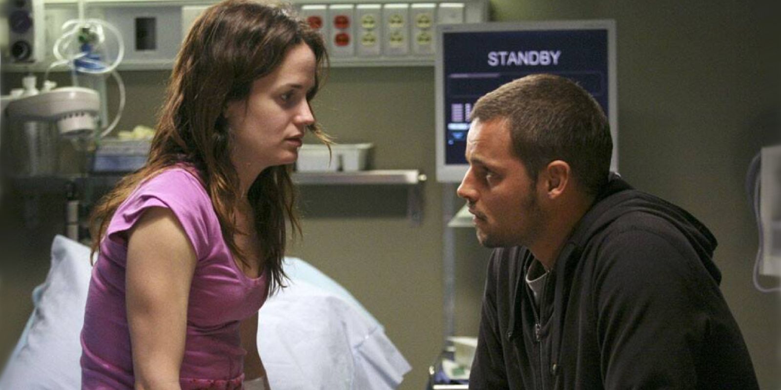 Ava/Rebecca está mirando a Alex mientras él se sienta junto a su cama en el hospital después de su intento de suicidio en Grey's Anatomy.