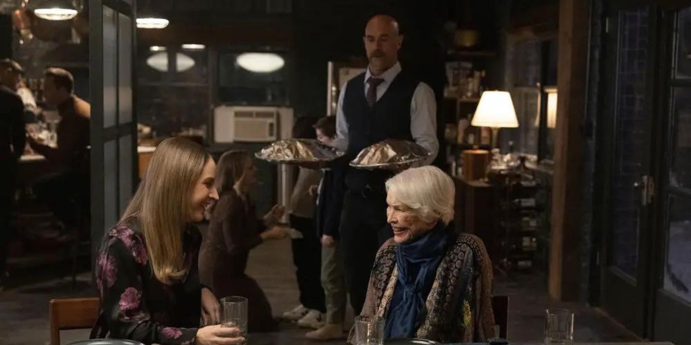 Allison Siko as Kathleen Stabler sits at a table with Ellen Burstyn as Bernie Stabler with Christopher Meloni as Elliot Stabler behind them on Law & Order_ Organized Crime
