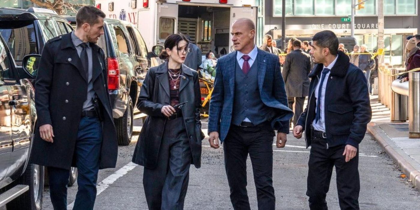 Brent Antonello as Jamie Whelan, Ainsley Seiger as Jet Slootmaekers, Christopher Meloni as Elliot Stabler, and Rick Gonzalez as Bobby Reyes waslk down the street with black cars and an ambulance behind them on Law & Order_ Organized Crime