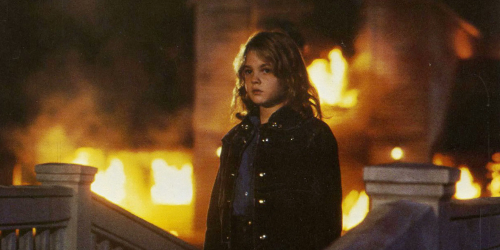 Drew Barrymore stands in front of a burning house in Firestarter
