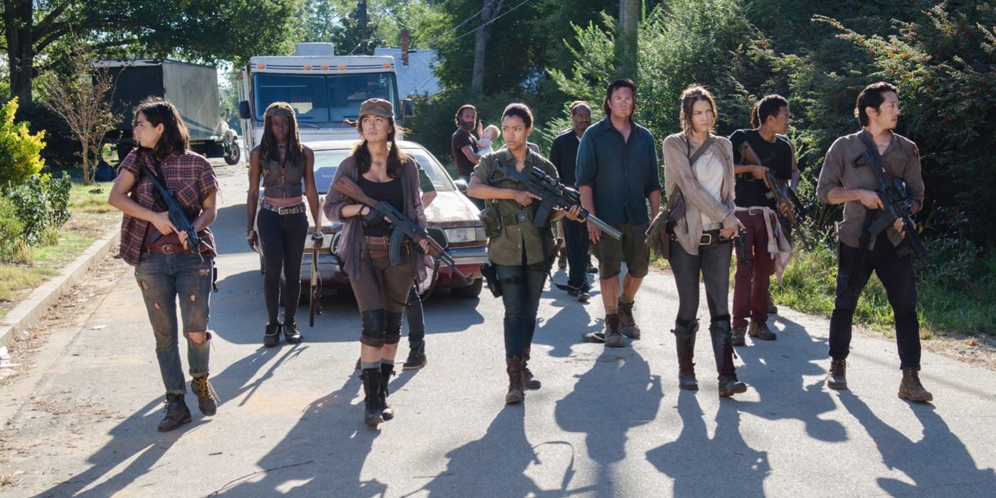 Elenco da 5ª temporada de The Walking Dead segurando armas na rua.