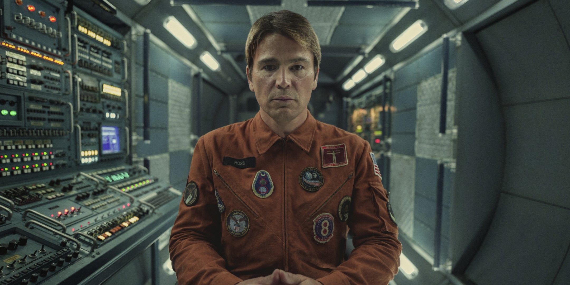David Ross (acto Josh Harnett) sits in an orange shirt in space in Black Mirror
