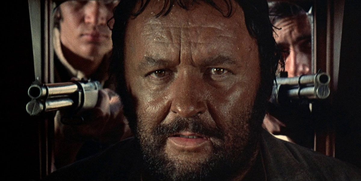 A close-up of Rod Steiger in between two rifles while riding in a carriage from Sergio Leone's Duck, You Sucker