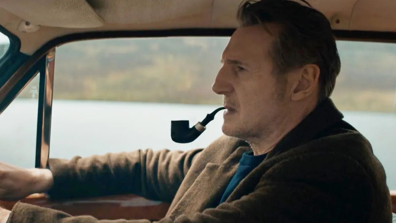 Liam Neeson smoking a pipe and driving in In The Land of Saints and Sinners