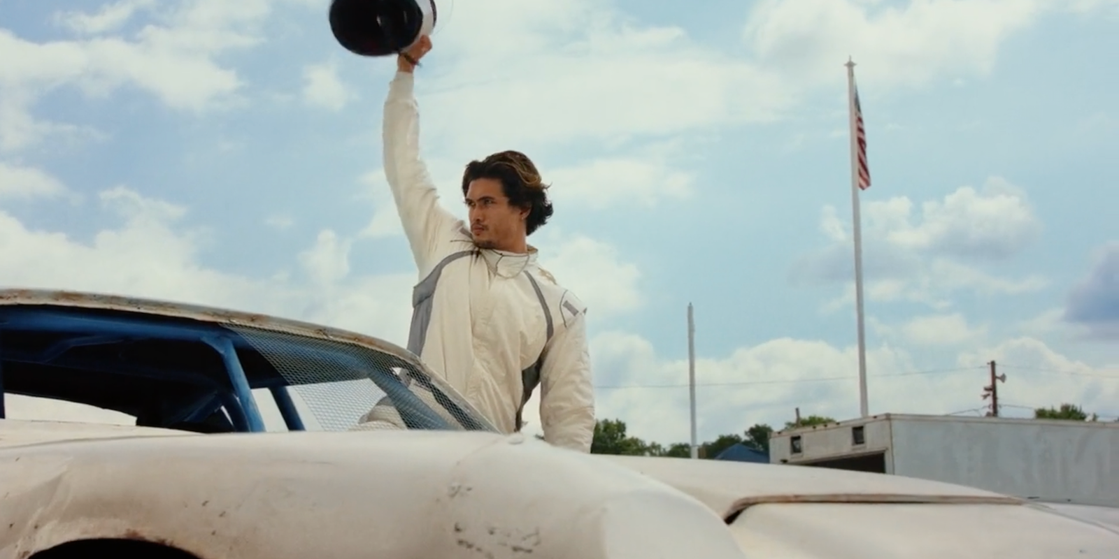 Charles Melton waving to the crown before getting into his race car in Poker Face