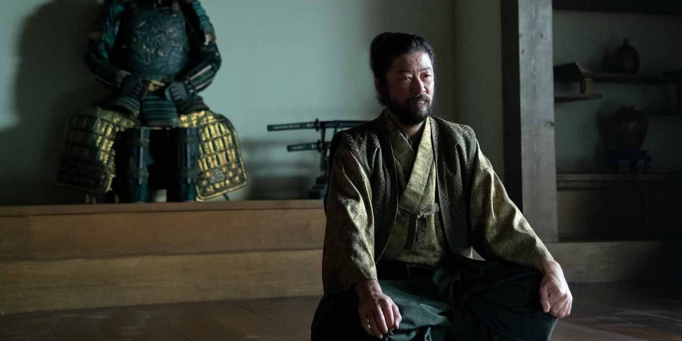 Yabushigue sits inside a palace with a samurai statue behind him