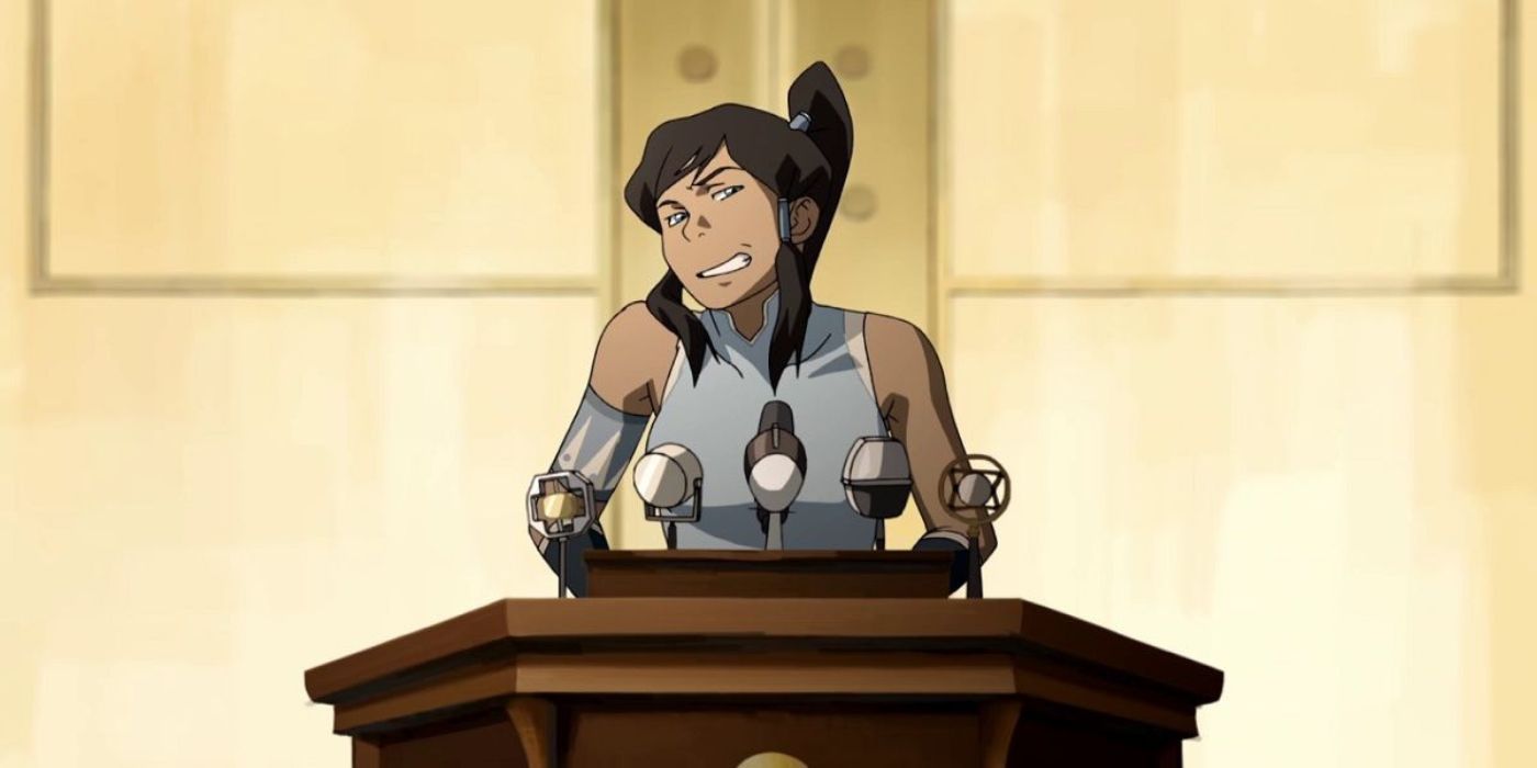 Korra wincing as she speaks to a crowd at a podium. 