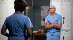 Lucas Adams (actor Niko Terho) stands against locker in scrubs in front of Simone on Grey's Anatomy