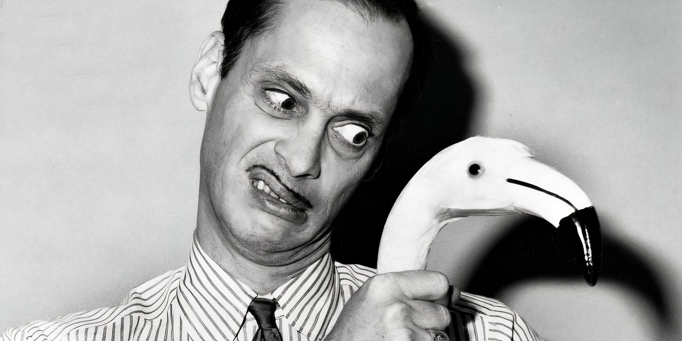 John Waters in black and white holding a flamingo