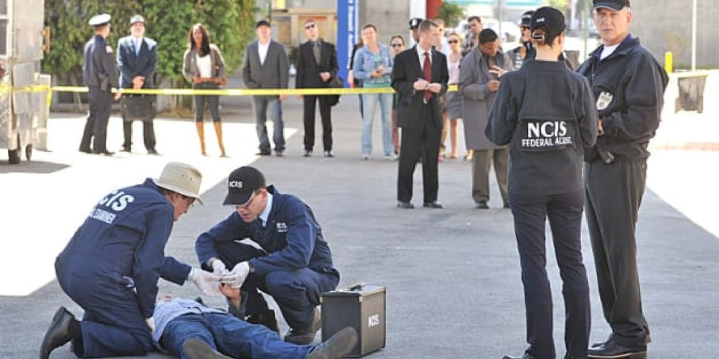 David McCallum as Ducky Mallard and Brian Dietzen as Jimmy Palmer crouch over a body while Cote de Pablo as Ziva David and Mark Harmon as Jethro Gibbs speak nearby on NCIS