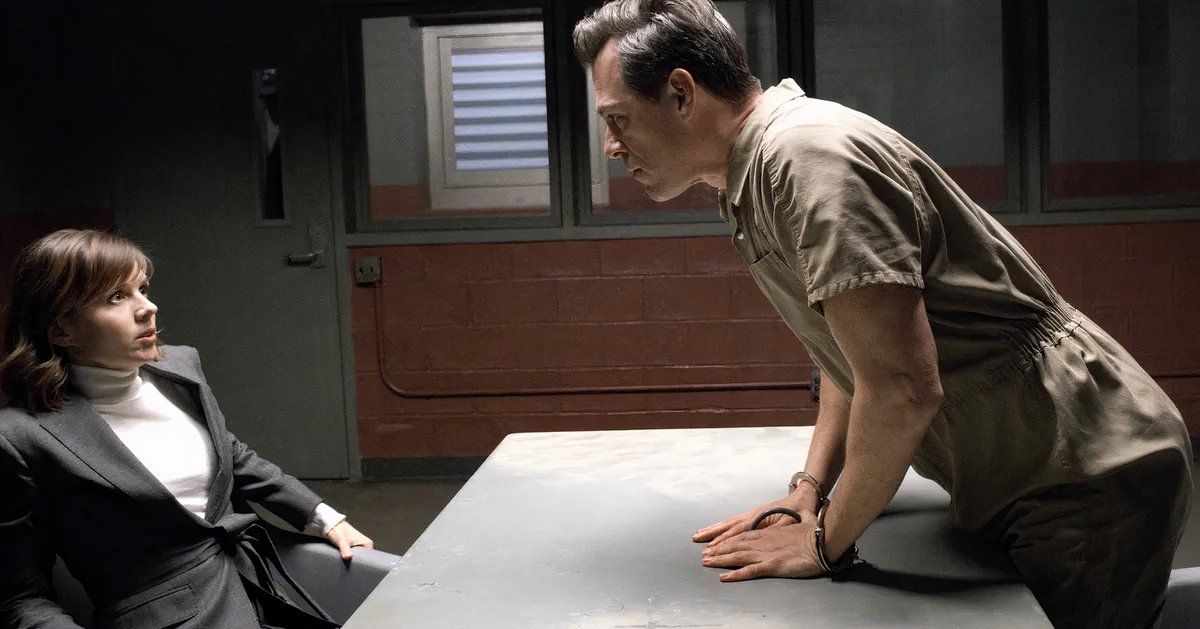 Darren Pettie como Orson LeRoux inclinando-se sobre uma mesa para ameaçar a assustada Dra. Kirsten Bouchard interpretada por Katja Herbers em Evil