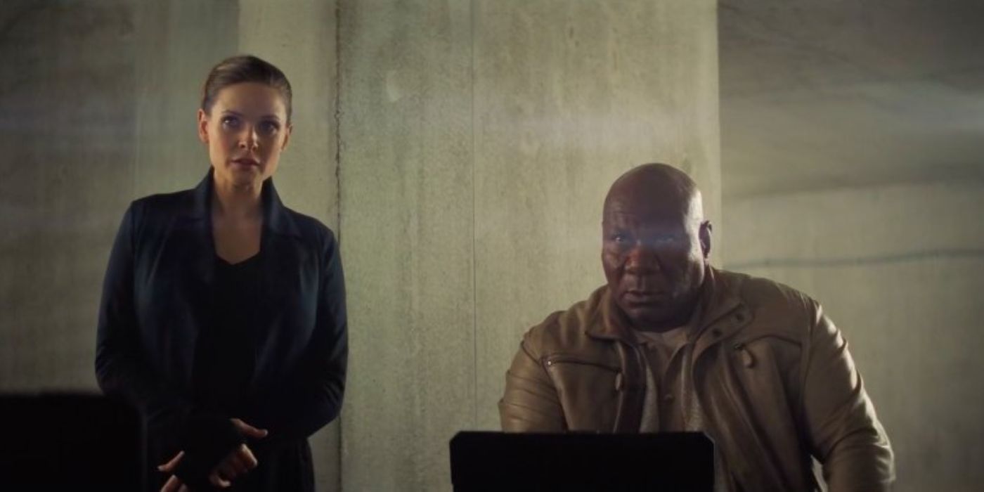 Ilsa stands next to Luther, who's working on his computer in Mission Impossible Fallout