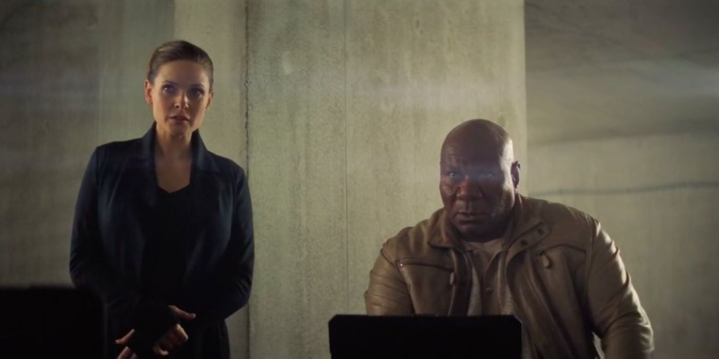 Ilsa está ao lado de Luther, que está trabalhando em seu computador em Mission Impossible Fallout.