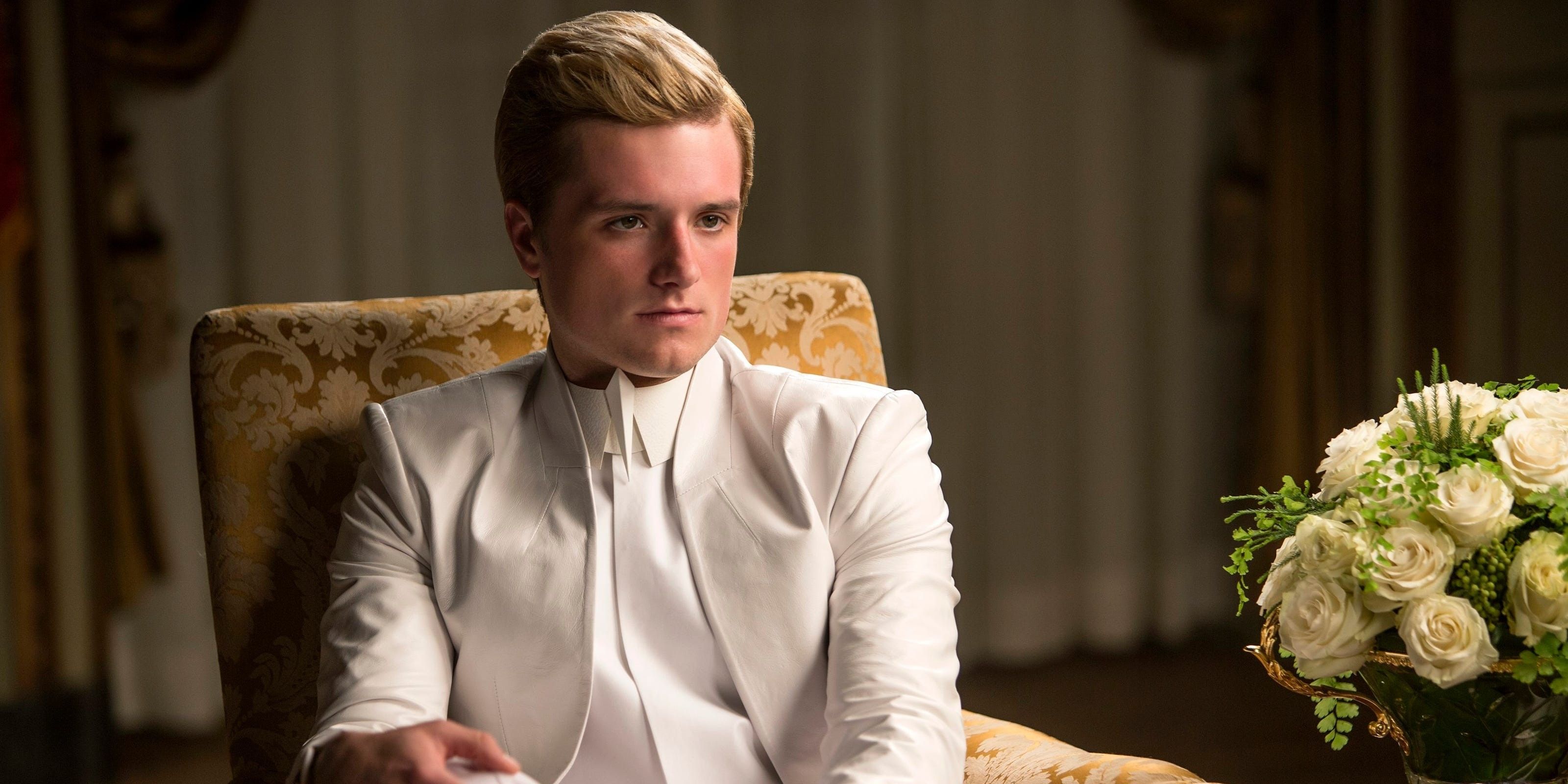Peeta Mellark sitting and wearing a white suit in The Hunger Games: Mockingjay Part 1.