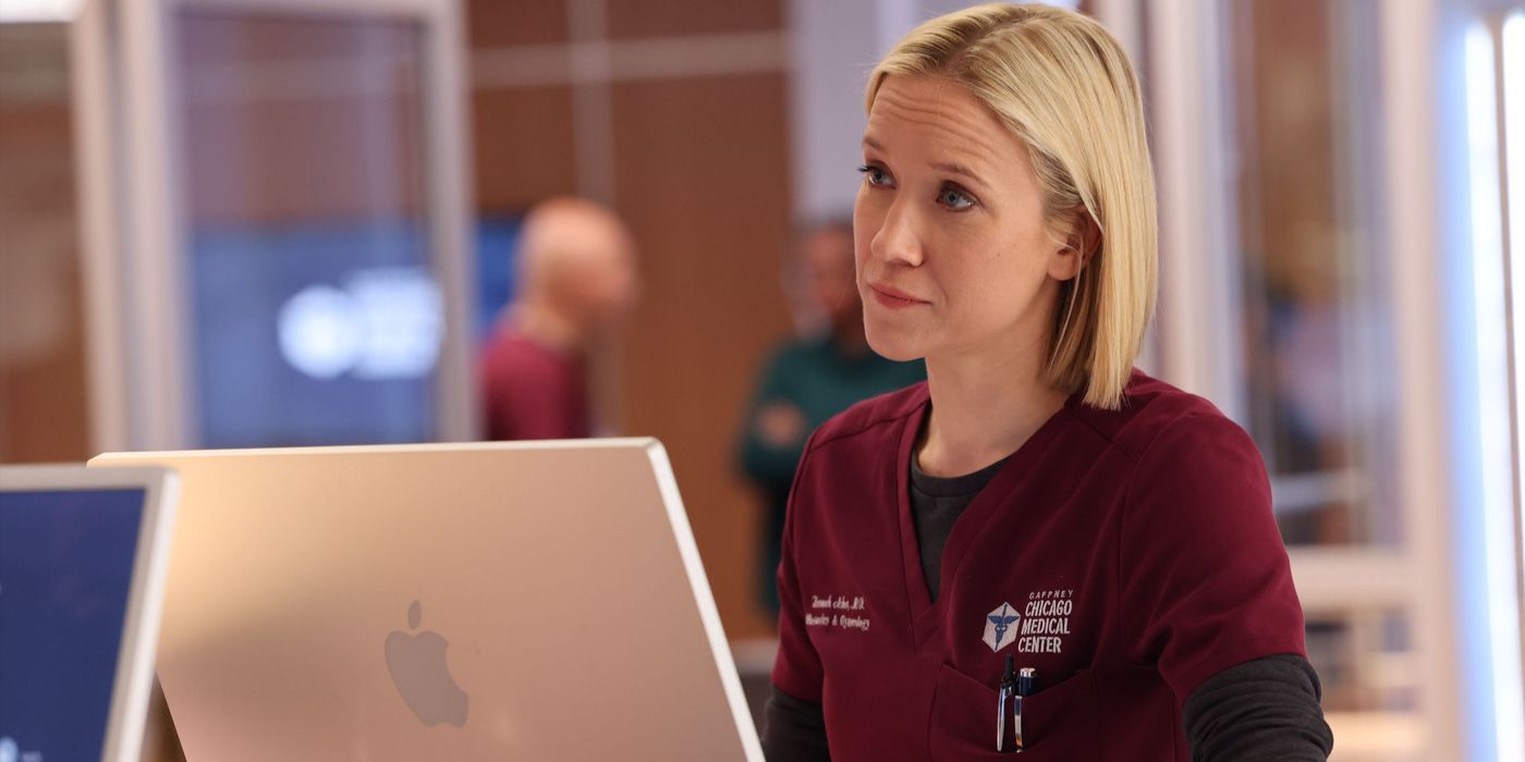 Hannah Asher (actor Jessy Schram) stands behind a computer in maroon scrubs on Chicago Med