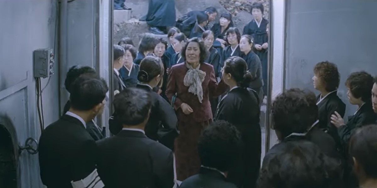 Madre de 2009 que muestra a Kim Hye-ja como la madre titular cuyo nombre no aparece en la película, rodeada por una multitud.