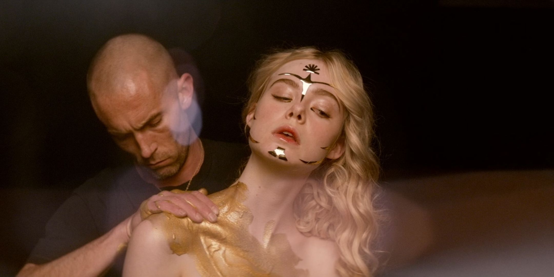 Desmond Harrington as Jack McCarther wipes gold paint on a heavily made-up Elle Fanning as Jesse in The Neon Demon