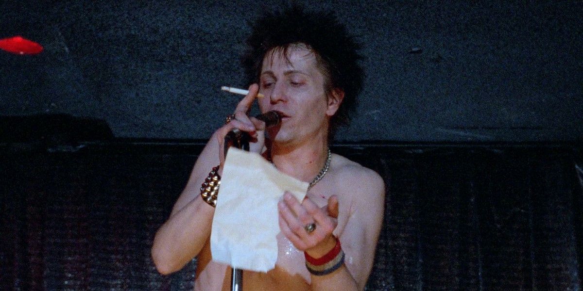 Gary Oldman, como o baixista do Sex Pistols Sid Vicious em Sid and Nancy, lê uma nota para a multidão.