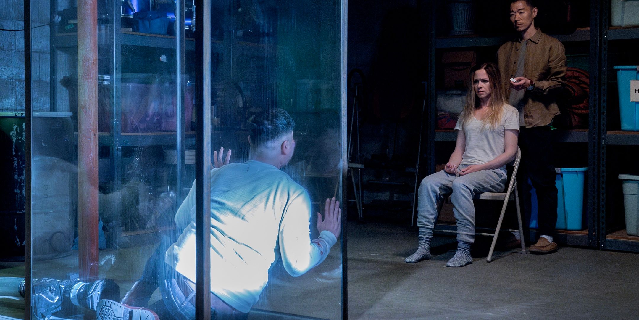 Jeremy Moy in the glass cage looking at Emma in a chair and Roger from Criminal Minds Evolution