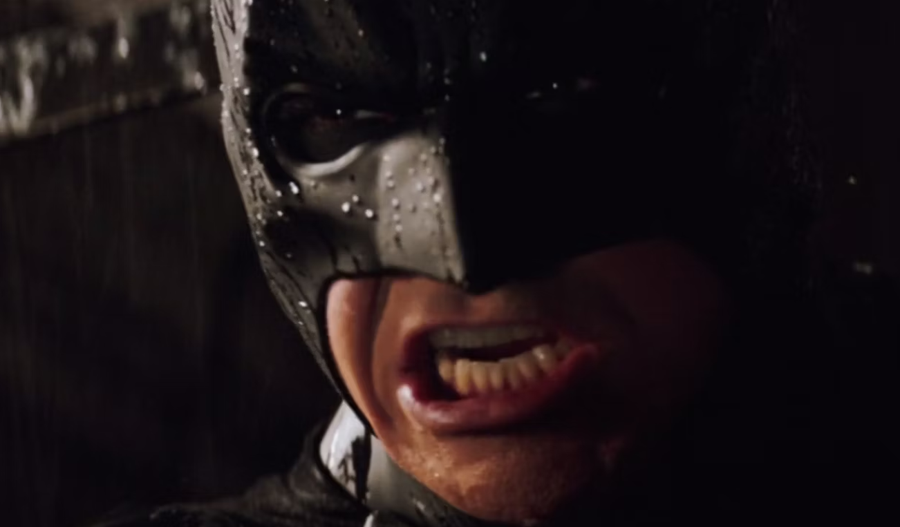 Um close mostra Batman (Christian Bale) fazendo uma careta enquanto fala com alguém.